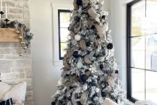 a flocked Christmas tree with black and white ornaments, striped and burlap ribbon, white snowflakes and a black star topper