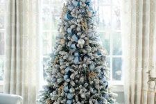 a flocked Christmas tree with dusty blue ornaments and ribbons is a chic and elegant decor idea