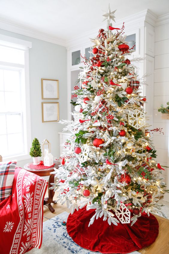 a flocked Christmas tree with greenery, red and white ornaments, lights, berries and plaid ribbon