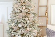 a flocked Christmas tree with lights, metallic ornaments, snowflakes and shiny mesh ribbons looks festive