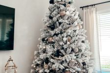 a flocked Christmas tree with wooden beads, snowflakes, branches on top and some black and metallic ornaments