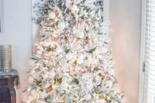 a flocked winter wonderland Christmas tree with white and silver ornaments, lights, red berries and greenery branches