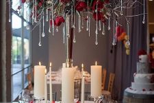 a glam Christmas chandelier with branches, evergreens, red roses, snowy pinecones and crystals as icicles