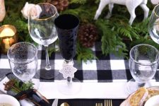 a lovely Christmas tablescape with a buffalo check runner and napkins, evergreens, pinecones, deer, candles and touches of gold for more chic