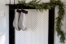 a minimalist faux fireplace with candles, simple grey stockings and an evergreen garland with lights