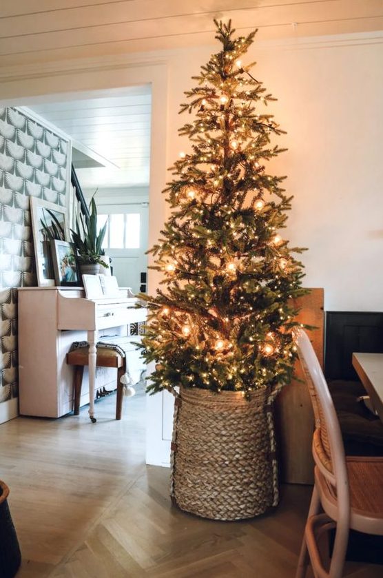 a pretty tall Christmas tree decorated with only lights and placed into a basket is a cool and fresh idea for a farmhouse space