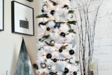 a white Christmas tree decorated with black and silver ornaments, evergreens, snowflakes, a wooden star topper
