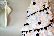 a white Christmas tree decorated with black and white ornaments, with snowflakes and lights plus a clear snowflake topper