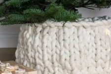 a white chunky knit cover for the tree base is a very creative and cool-looking idea to hide an eye-sore and make your tree more holiday-like