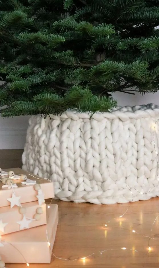 a white chunky knit cover for the tree base is a very creative and cool-looking idea to hide an eye-sore and make your tree more holiday-like