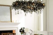 an elegant holiday chandelier with greenery, lights, silver and crystal ornaments is perfect for the holidays