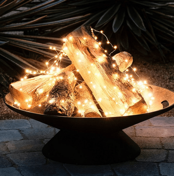 a metal bowl with firewood and string lights to imitate a fire