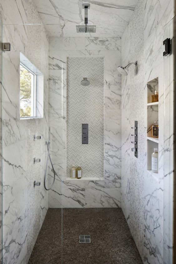 marble walk-in shower with a different floor and built-in shelves