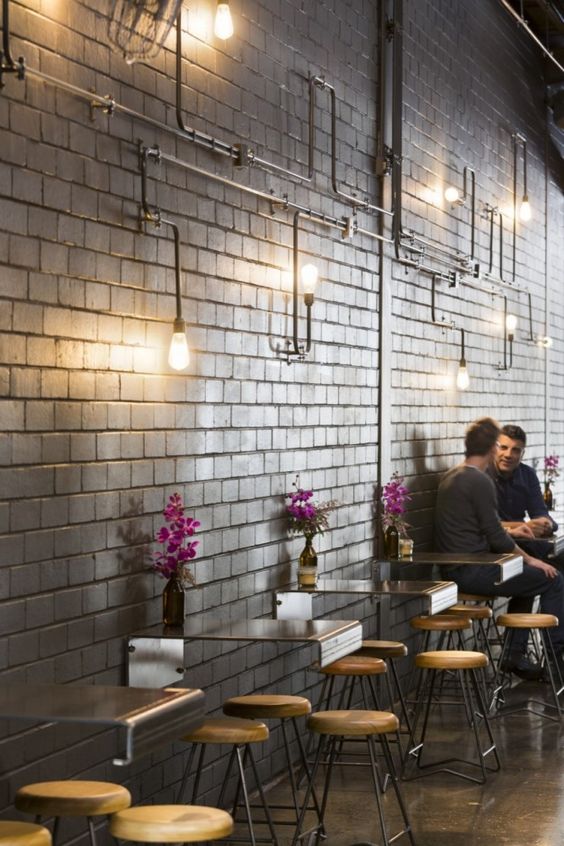 industrial coffee shop with metal tables attached to the walls and exposed pipes with bulbs