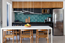 07 The kitchen is modern and dynamic, with matte black and warm wood cabinets, tube lights and emerald geo tiles