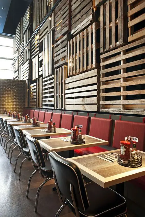 pallets cover the wall and contrast with red chairs and retro tables
