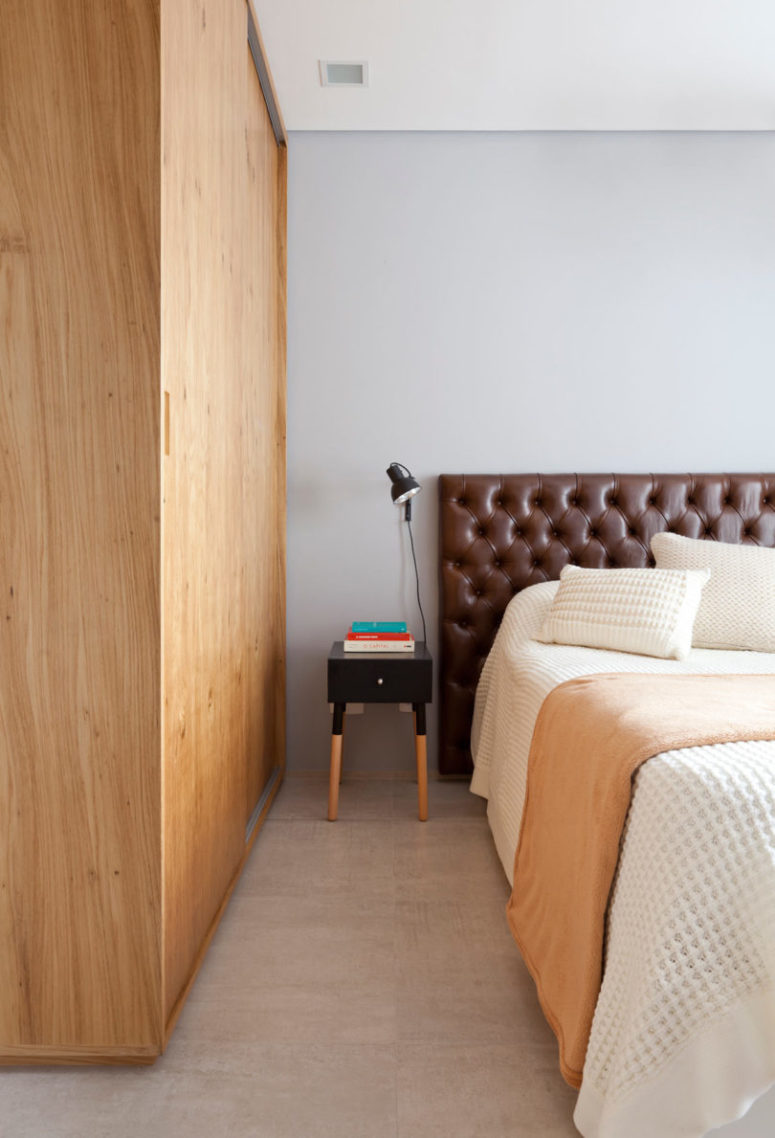 The bedroom has simple and cozy design, with a warm wood wardrobe, a leather headboard and warm-colored touches
