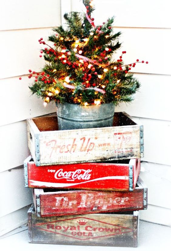 a small tree with lights and berries in a glavanized bucket and crates