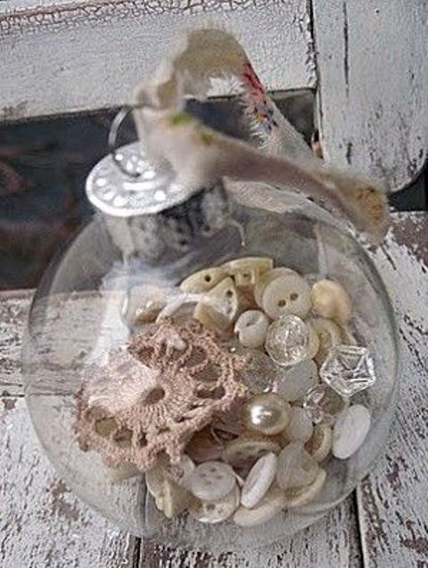 a transparent glass ornament filled with buttons, pearls and lace