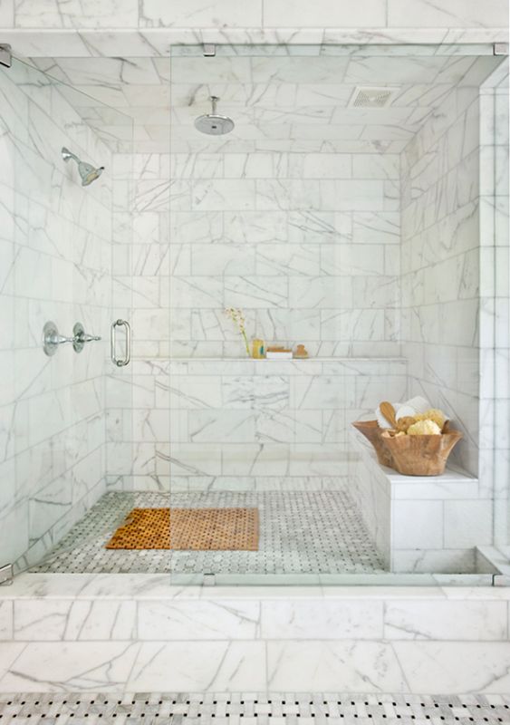large marble shower and steam room in one with shelves and a bench