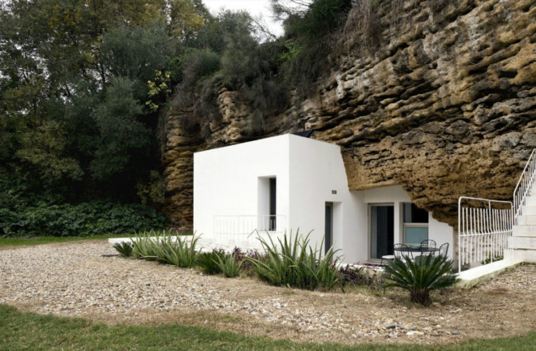 White plaster house architecture looks spotless next to discolored rock and there's a lot of greenery around