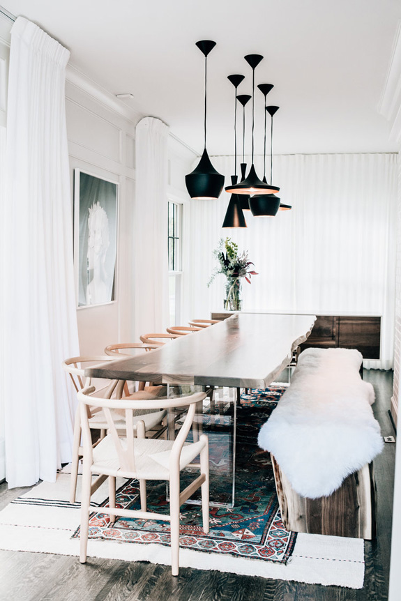 This is a dining zone with a raw-wood edge dining table with acrylic legs, a fur covered bench and lots of lights