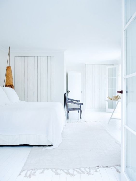 The relaxed all-white master bedroom makes you feel already on the beach, and I love the shabby blue seat
