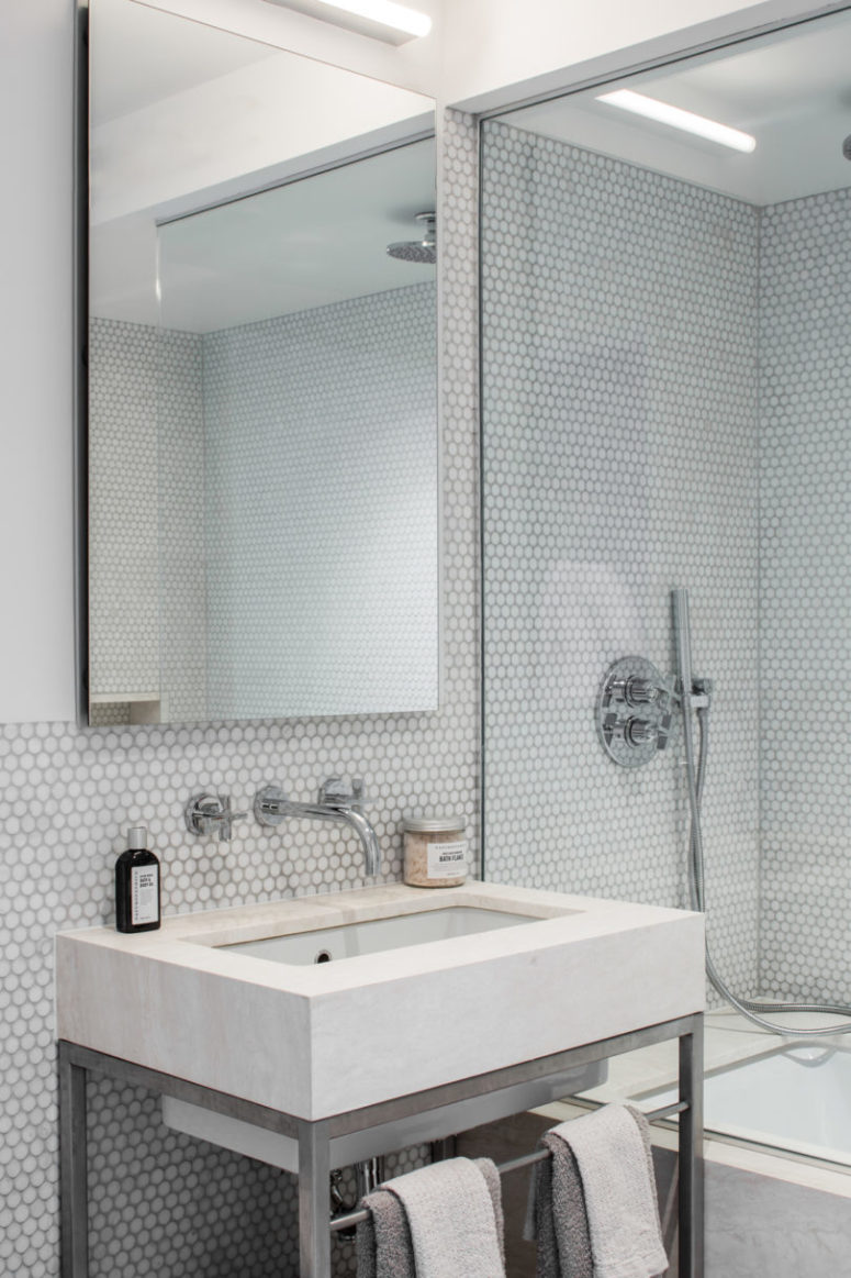 The bathroom is a large modern one, with white penny tiles, nickel faucets and some concrete