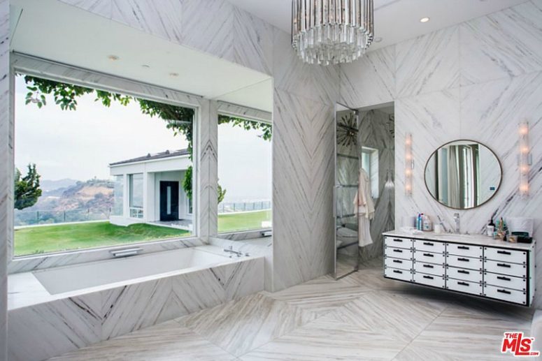 The master bathroom is clad with light-colored marble, the design is totally glam