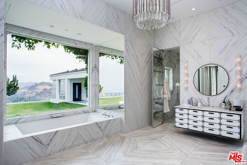The master bathroom is clad with light colored marble, the design is totally glam