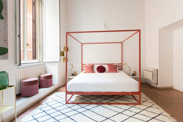 A red four poster bed can make a statement in any neutral interior. Some other bright elements, like pink poufs, a bright green vase with some greenery and a diamond patterned rug also makes the bedroom's design quite eye-catchy. (Giulia Venanzi)