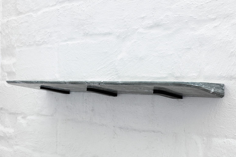 The marble is precisely fixed to three small wedges that fasten to the wall, locking into the stone using only gravity