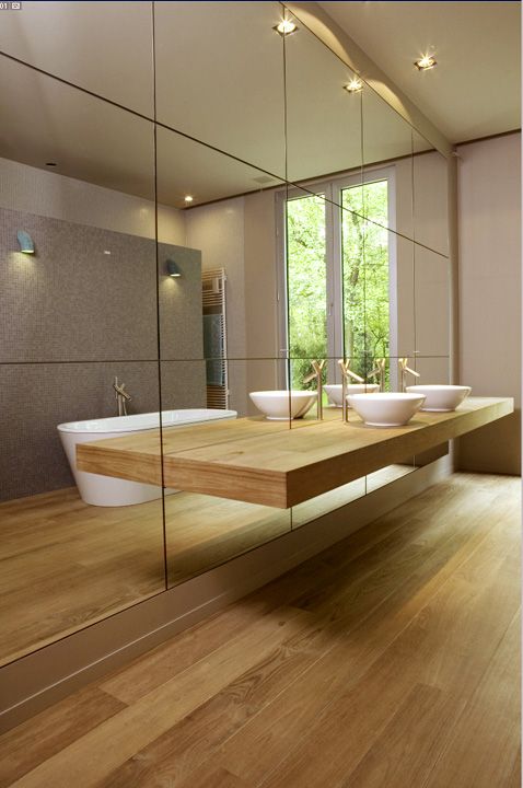 Minimalist bathroom with light colored wood and a mirror wall and a thin counter not to spoil the look