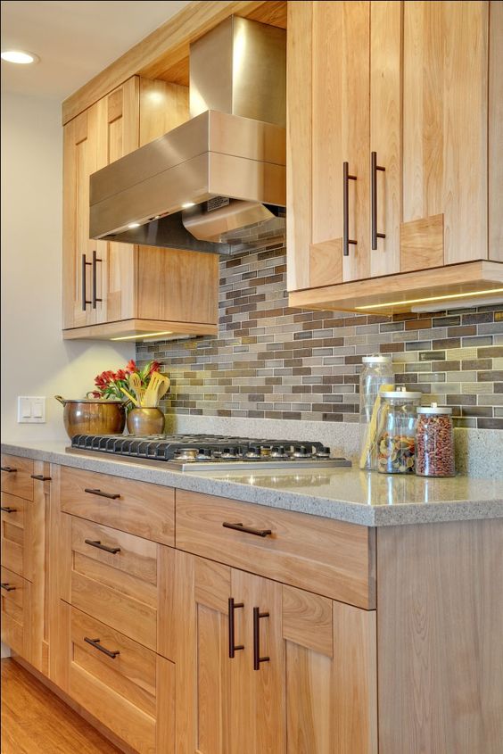 Light colored kitchen cabinets with a earth tone backsplash and a grey quartz counter