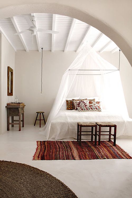 a boho chic inspried bedroom with a bed with a canopy frame attached to the ceiling