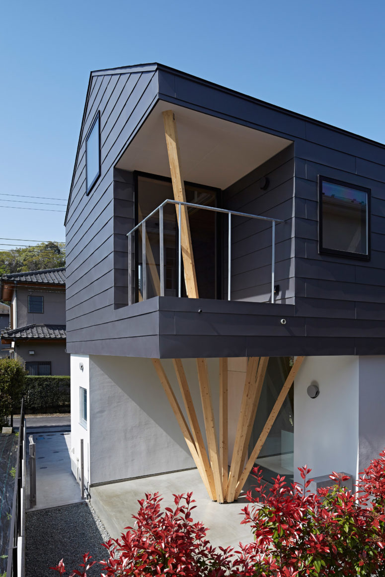 This modern dark house features clusters of wooden columns that fulfill many functions