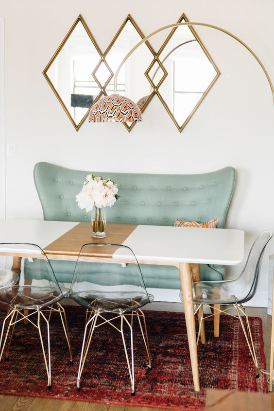 a color blocked dining table in black and copper with wooden legs looks cute with acrylic chairs and a mint love seat