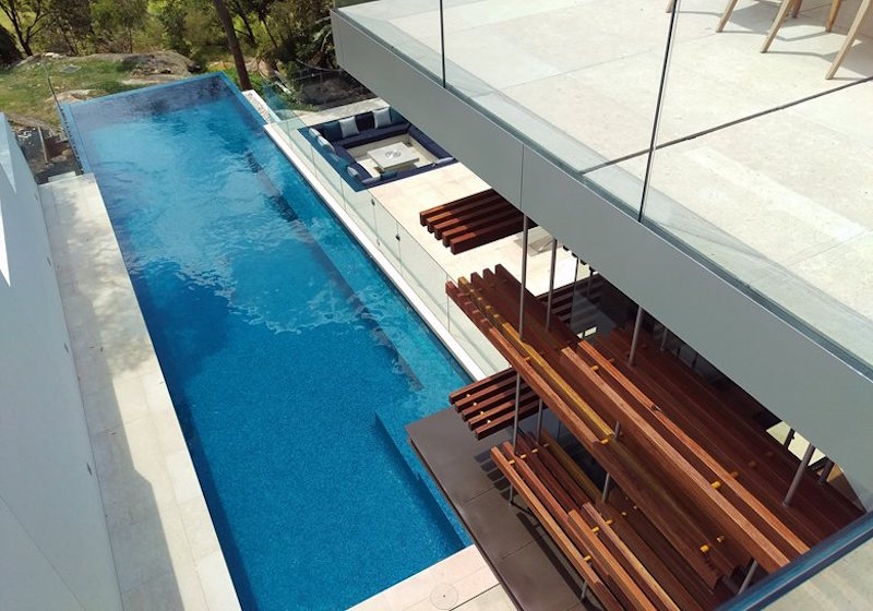 A long, rectangular swimming pool extends and cantilevers over the edge of the slope
