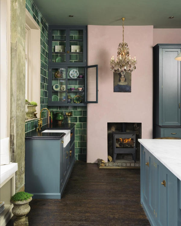 An antique metal hearth looks creative with a pink wall, and a vintage portrait adds a glam feel