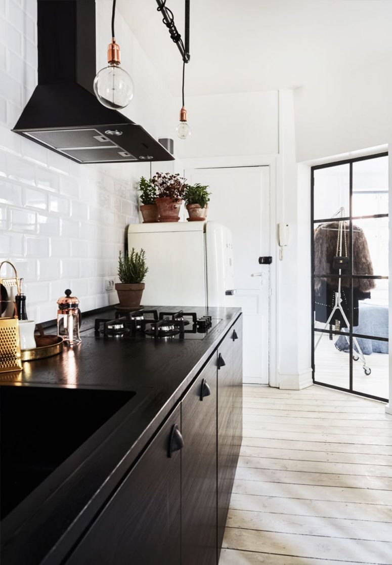 The kitchen features black cabinets, industrial bulbs over them and a white tile backsplash