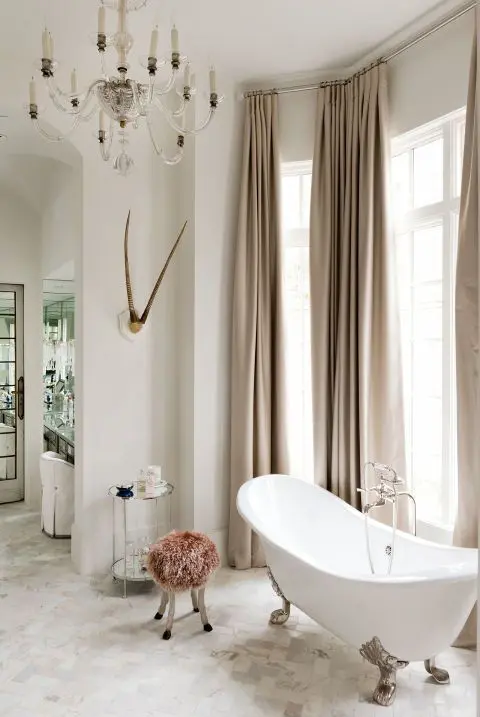 a feminine space with beige curtains, a pink stool and a refined oval bathtub on nickel legs