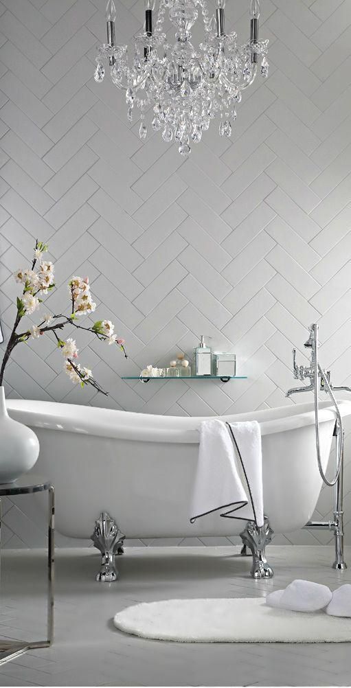 a modern chic bathroom with a clawfoot tub, herringbone tiles and a gorgeous crystal and silver chandlier