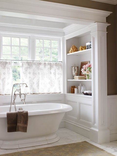 a cool freestanding tub in a niche, half curtains for privacy and shelves on each side of the bathtub
