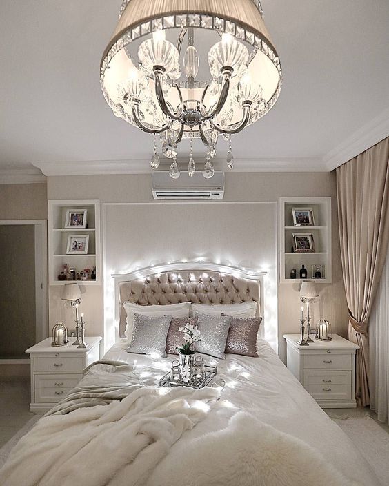 a neutral and refined bedroom with a vintage-inspired chandelier with crystals and a fabric lampshade