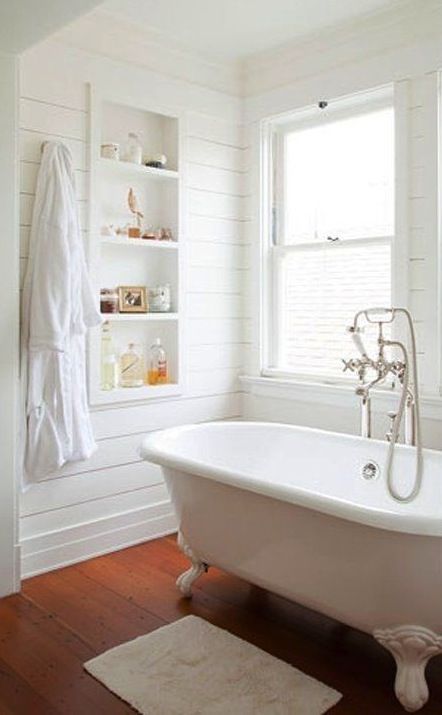 all-white bathroom with wooden floors for a rustic feel, a white tub with white legs