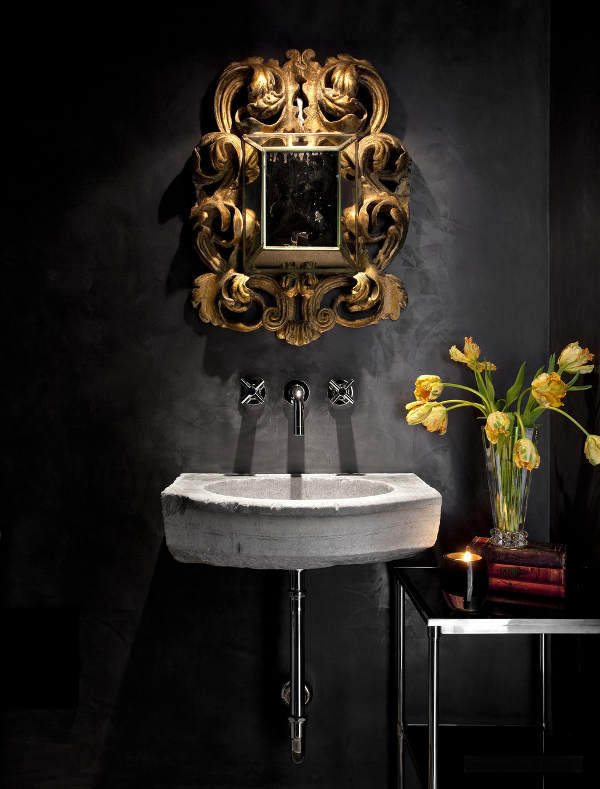 The bathroom is done in black, with a concrete sink and a refined gold frame mirror