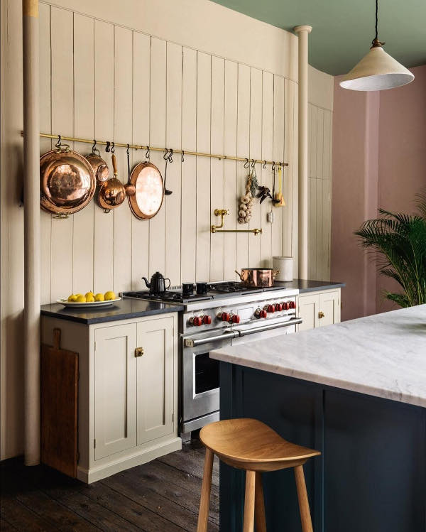 There's a creamy wall covered with wood, with several cabinets of the same color and a holder with copper pans