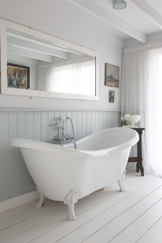 serene bathroom with a white bathtub on clawfoot legs and whitewashed wooden floors