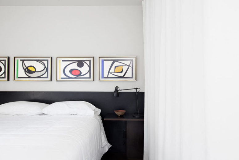 The bedroom features a dark colored bed and abstract artworks