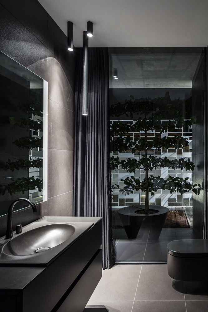 The bathroom is dark and moody, with a tree and dark walls and appliances